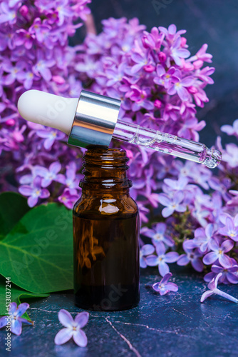 Essential oil of lilac flowers on a dark marble background, vertical photo