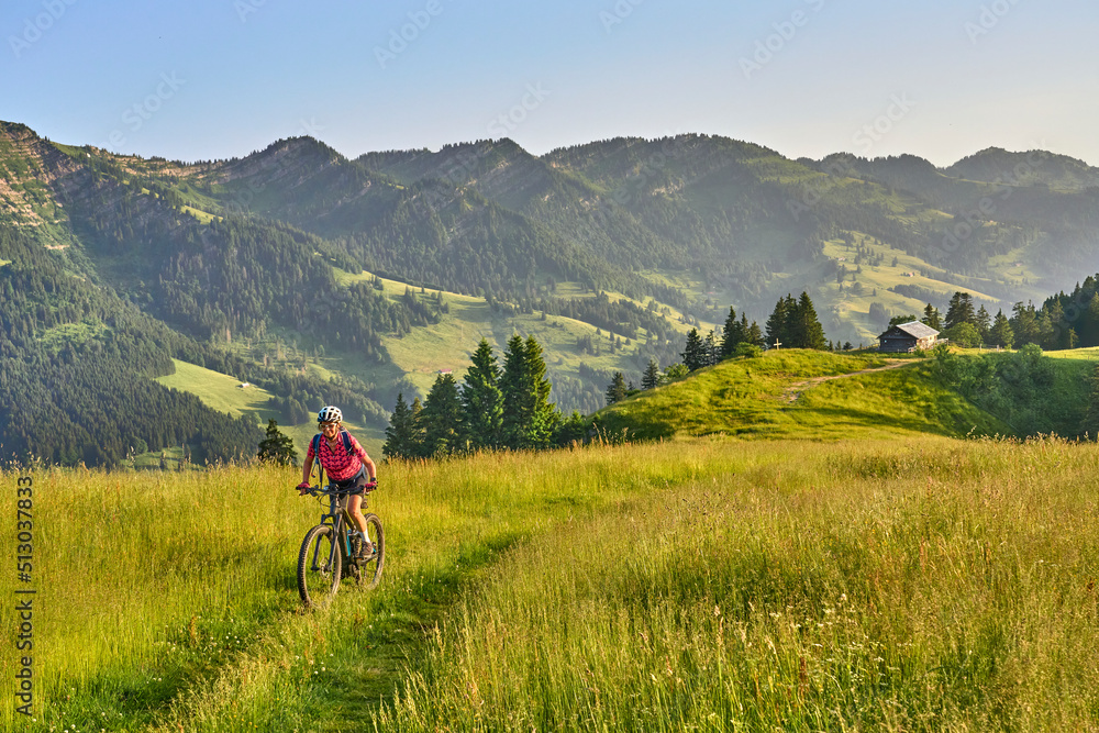 pretty senior woman riding her electric mountain bike on the mountains above Oberstaufen with Nagelfluh mountain chain in background, Allgau Alps, Bavaria Germany