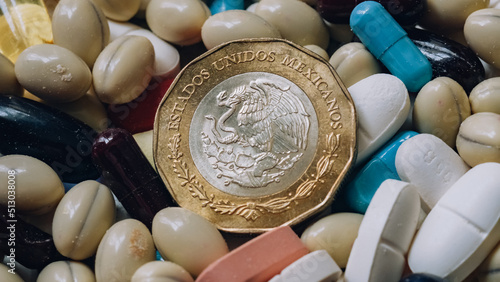 Photo of a 10 Mexican peso coin among pills of many shapes and colors that could probably be used to illustrate the economics of the pharmaceutical industry or drug trafficking in Mexico.
