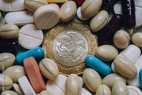 Photo of a 10 Mexican peso coin among pills of many shapes and colors that could probably be used to illustrate the economics of the pharmaceutical industry or drug trafficking in Mexico.