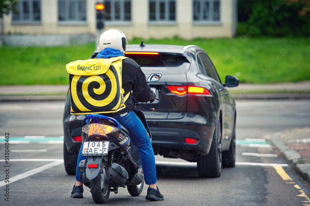 Minsk, Belarus. Jun 2022. Food delivery man rides motor bike with yellow bag. Yandex Food