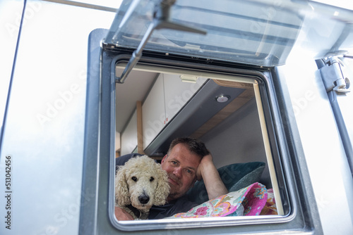 Mann liegt mit seinenem Hund im Wohnmobil auf dem Bett und schaut aus dem Fenster