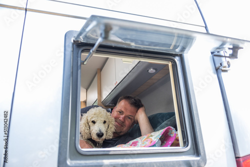 Mann liegt mit seinenem Hund im Wohnmobil auf dem Bett und schaut aus dem Fenster photo