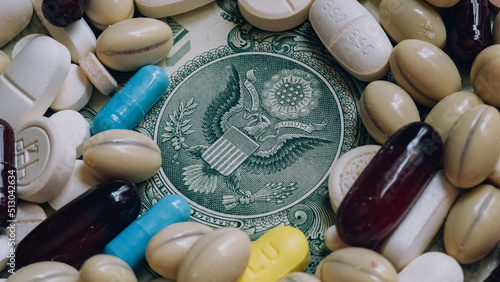 Photo of a US one dollar bill among pills of many shapes and colors that could probably be used to illustrate the economics of the pharmaceutical industry  in the United States of America.