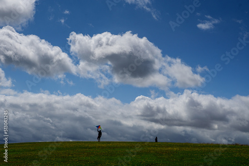 People silhouetted against a blue cloudy sky launching a kite on the Yorkshire coastline © jmh-photography