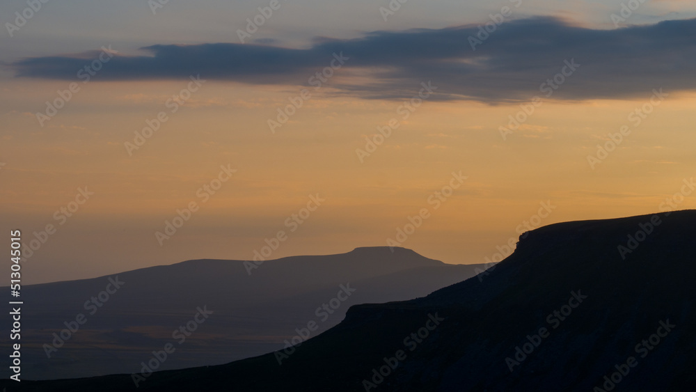 Sunsets of the distinct silhouette of Penyghent one of three hills that make up the Yorkshire 3 Peaks with its sister in the background Ingleborough