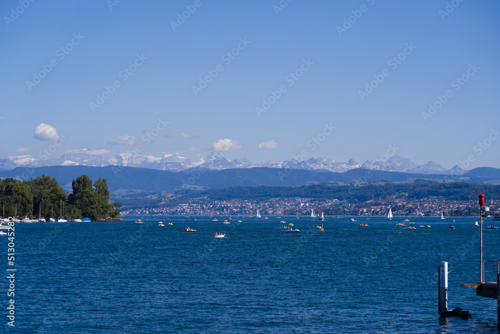 Naklejka premium Scenic landscape with Lake Zürich, leisure boats and Swiss Alps in the background on a sunny summer day seen from City of Zürich. Photo taken June 11th, 2022, Zurich, Switzerland.