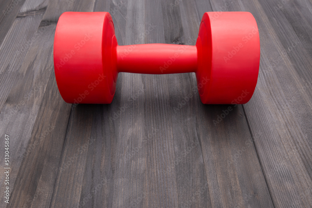 Obraz premium One red dumbbell on dark gray wooden surrface