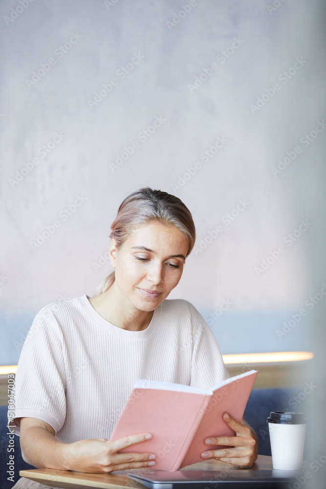 Content curious young lady sitting at table with coffee cup and spending time with interesting book Content curious young lady sitting at table with coffee cup and spending time with interesting book