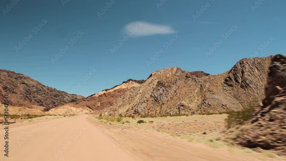 Traveling in the desert. Point of view of a car driving along the dirt route across the arid environment, rock and sandstone mountains, under a blue sky. Traveling in the desert. Point of view of a car driving along the dirt route across the arid environment, rock and sandstone mountains, under a blue sky.