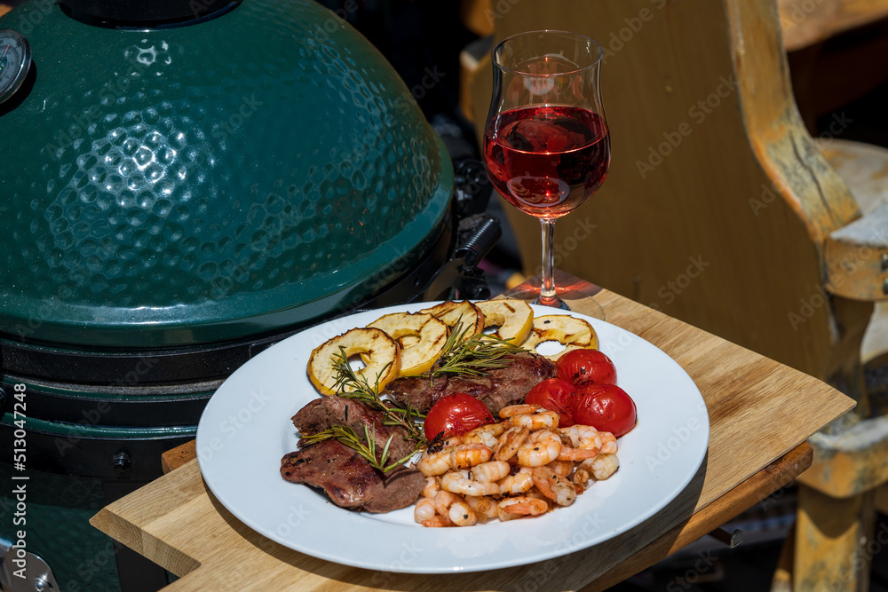 grilled shrimps, venison meat, cherry tomatoes and apple rings  from a bbq grill at a sunny summer day on the balcony