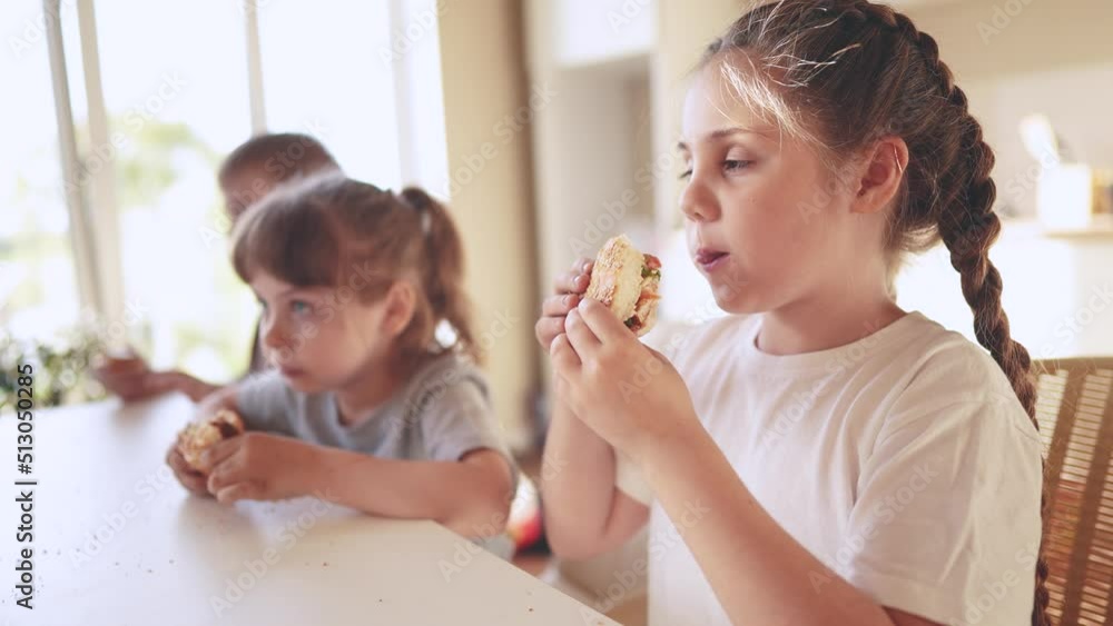 children eat burgers. fast food burger. a group of small children in the kitchen greedily eat fast food burgers. big family small kids sun having breakfast in the morning in the kitchen eating burger