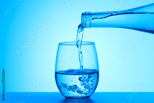Crystal clear water pouring into the glass on a blue background. Quality water for your health concept.