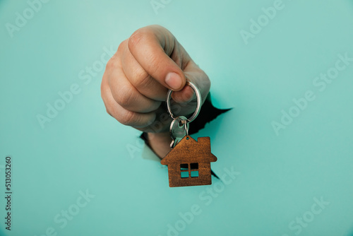 Man's hand with house key through a hole in blue background. House sale and rent concept