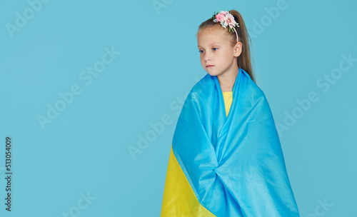 Portrait of upset patriot child girl with Ukrainian flag on blue studio background photo