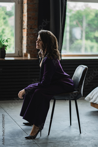 a young brunette woman in a purple pantsuit on the background of the window 