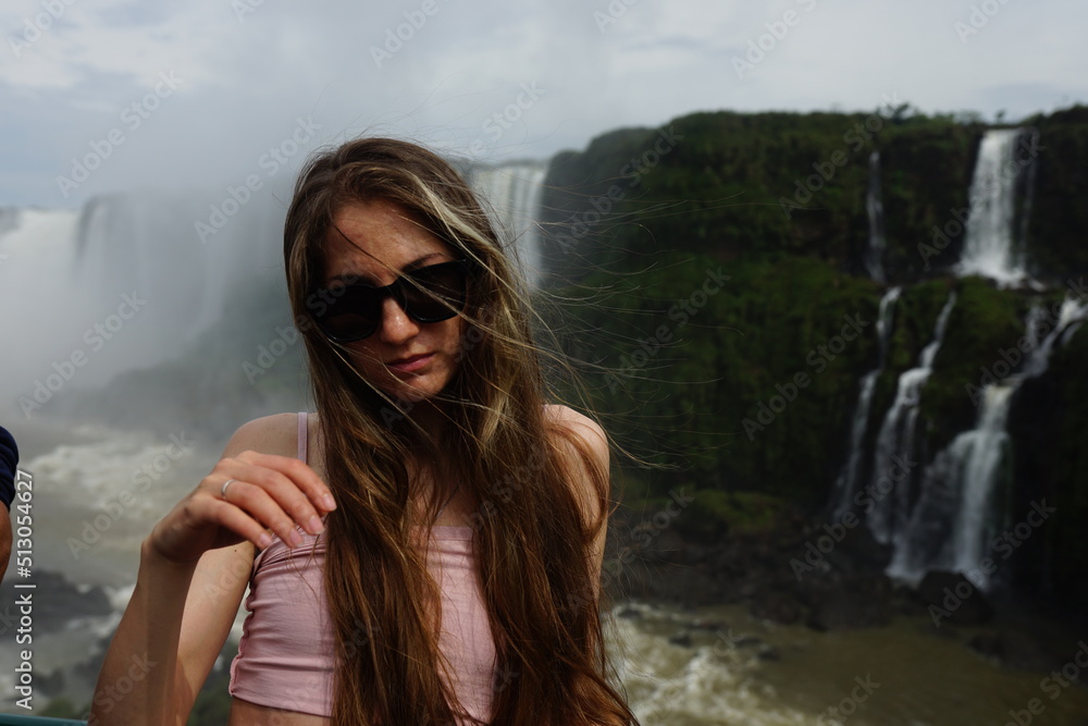 In the photo, the girl poses against the backdrop of Iguazu Falls — a ...