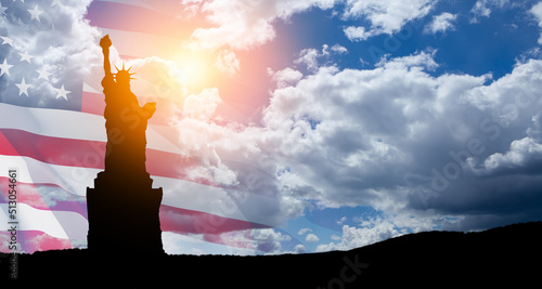 Statue of Liberty with a large american flag and blue sky on background.