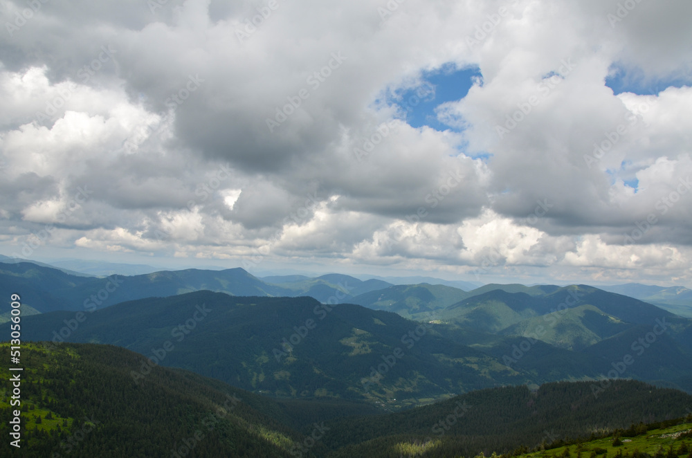 Low cloudy sky over the mountain peaks covered with dense forest. Carpathian mountains, Ukraine. Travel background.