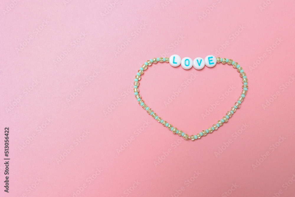 a beaded bracelet with the inscription love on a pink background with a copy space.