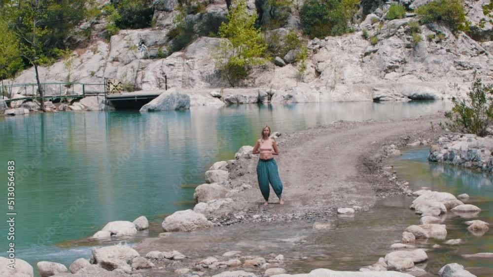 A woman in wide pants performs simple gymnastics by the lake A woman in wide pants performs simple gymnastics by the lake