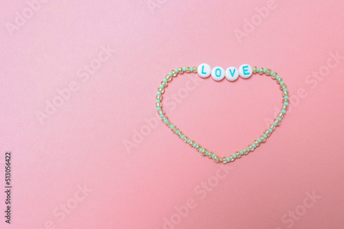 Картината върху платно a beaded bracelet with the inscription love on a pink background with a copy space