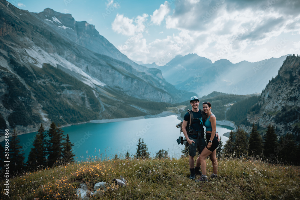 Un couple qui est en montagne lors d'une randonnée et qui regarde le magnifique panorama, avec un lac, des chemins et une forêt.