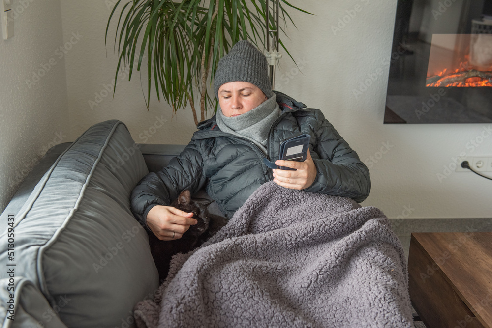 Fototapeta premium Woman sitting at home with jacket freezing saves energy