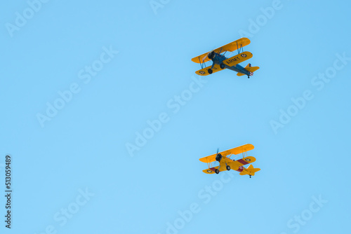 Two biplanes in formation over an airfield during an airshow.