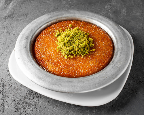 Turkish dessert kunefe, kunafa, kadayif with pistachio powder and cheese, served hot, very sweet. Turkish traditional dessert on grey background photo