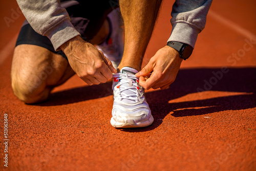Runner man tying shoelace in the stadium  cross training workout. Sporty male training outside