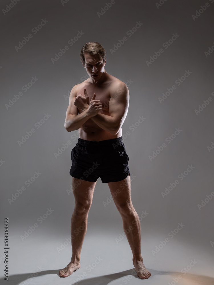 Obraz premium young muscular man in an expressive pose, artistic pose of the hero with outstretched arms. Beautiful muscles. extraordinary athletic body. Portrait on a gray background