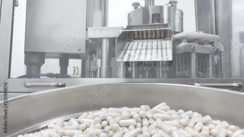 White capsules pills moving on metal automatic line in workshop of pharmaceutical factory. Closeup view of drugs move along conveyor belt during work process in pharma chemical company.  photo