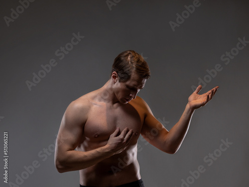Muscular man in an artistic pose, portrait on a gray background. The guy is an athlete with spectacular muscles in a dramatic pose.