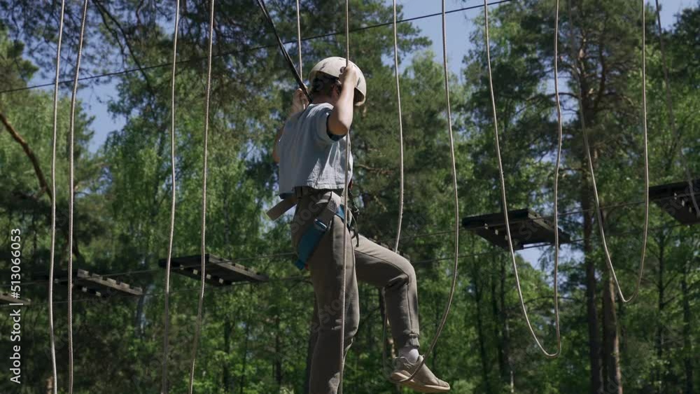 Entertainment and tourism concept. A brave teenage girl overcomes difficult obstacles by walking on a rope stretched between tall trees in a rope town. Entertainment and tourism concept. A brave teenage girl overcomes difficult obstacles by walking on a rope stretched between tall trees in a rope town.