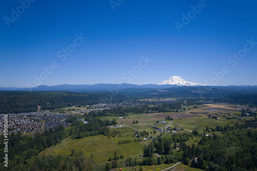 An aerial view of Puyallup, Washington with Mt. Rainier covered in snow under a clear blue sky in the background.