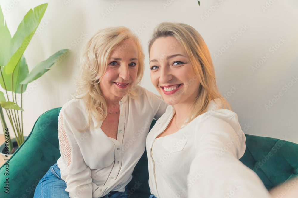 Horizontal indoor shot in an apartment of two blonde well-dressed attractive millenial female siblings sitting on a dark-green couch. High quality photo Horizontal indoor shot in an apartment of two blonde well-dressed attractive millenial female siblings sitting on a dark-green couch. High quality photo