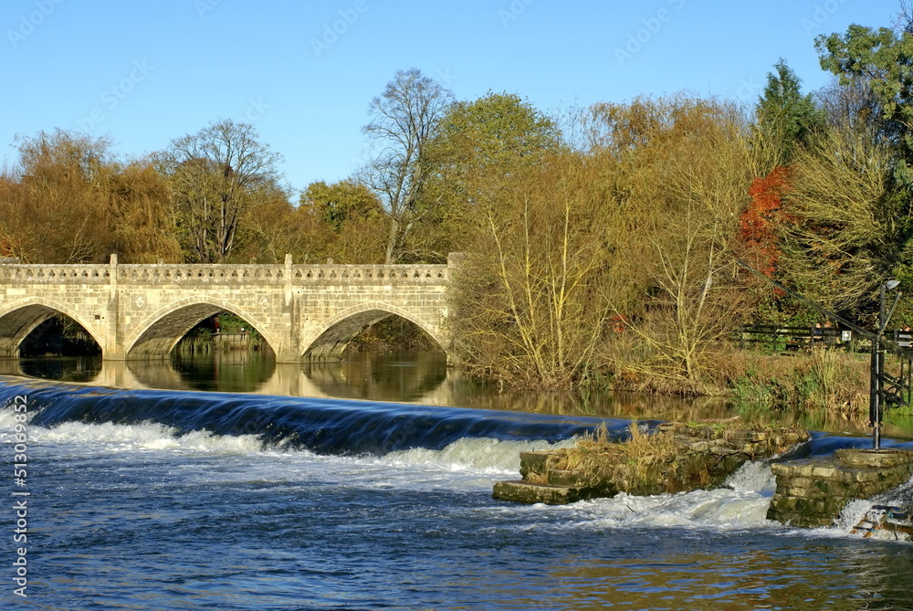 Fototapeta premium Autumn foliage around a bridge above a dam on the River Avon in Bath, England, UK