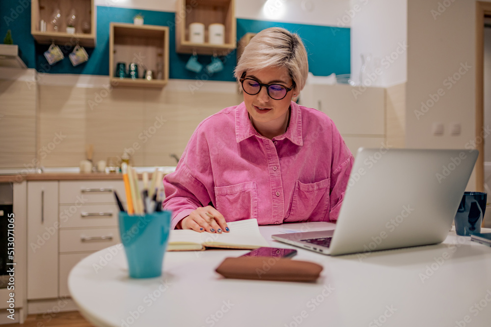 Woman with short hair working on a laptop at home and writing notes Woman with short hair working on a laptop at home and writing notes