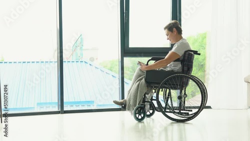 Mature woman sitting on the wheelchair reading a book at home photo