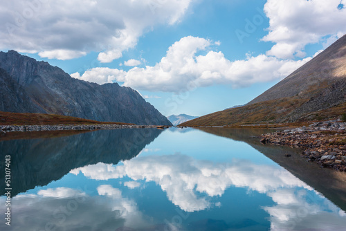 Tranquil autumn landscape with clouds reflection on smooth mirror surface of mountain lake in high hanging valley. Meditative view from calm alpine lake to mountain vastness. Glacial lake clear water.