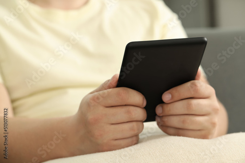 Man using e-book reader indoors, closeup view