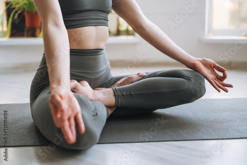 Young fit woman practice yoga doing asana lotus position in light yoga studio with green house plant