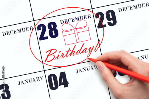 The hand circles the date on the calendar 28 December, draws a gift box and writes the text Birthday. Holiday. photo