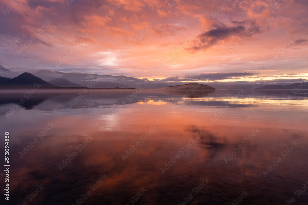 雲を染める幻想的な日没の空を湖面に映す黄昏の湖。日本の北海道の屈斜路湖。