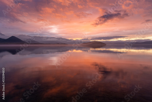 雲を染める幻想的な日没の空を湖面に映す黄昏の湖。日本の北海道の屈斜路湖。