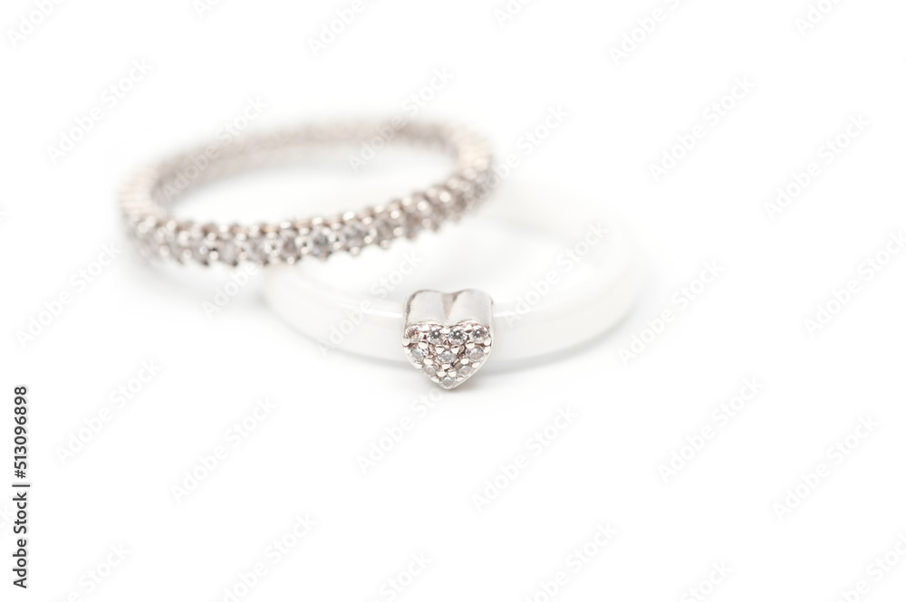 A white ceramic ring with a metal heart decorated with rhinestones and a silver ring with decorative stones. A white ceramic ring with a metal heart decorated with rhinestones and a silver ring with decorative stones.