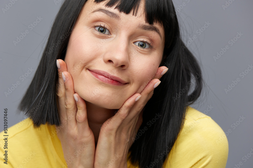 a happy, joyful woman stands on a gray background and holds her hair with her hands, smiling broadly a happy, joyful woman stands on a gray background and holds her hair with her hands, smiling broadly
