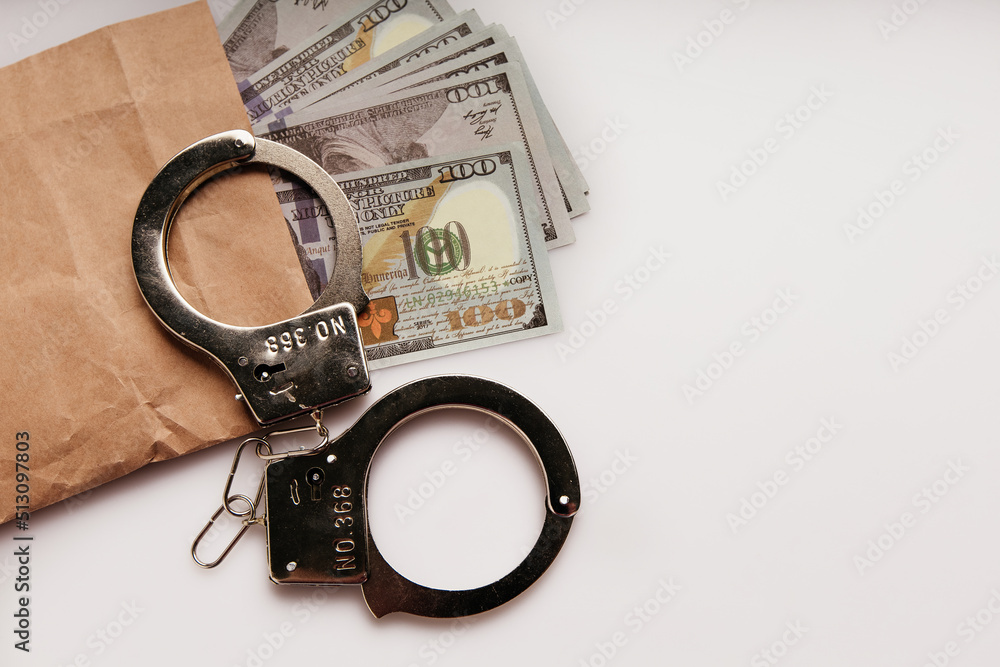 Envelope with dollars and handcuffs on a white background. Bribe and financial fraud concept Envelope with dollars and handcuffs on a white background. Bribe and financial fraud concept