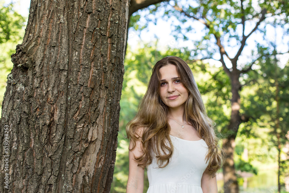 Beautiful young Russian girl dressed in a white dress, walks through the forest among the oaks in the rays of the sunset Beautiful young Russian girl dressed in a white dress, walks through the forest among the oaks in the rays of the sunset